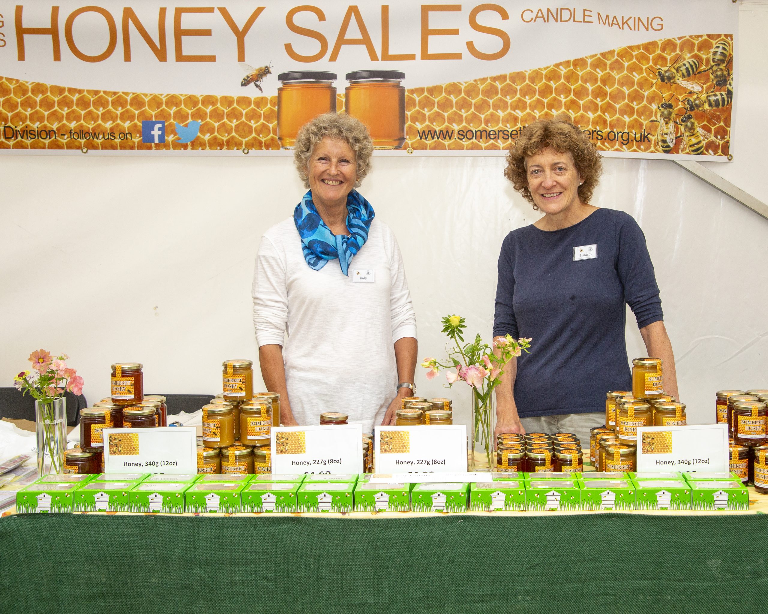 Two ladies standing behind a table selling Honey in the Bees and Honey Tent