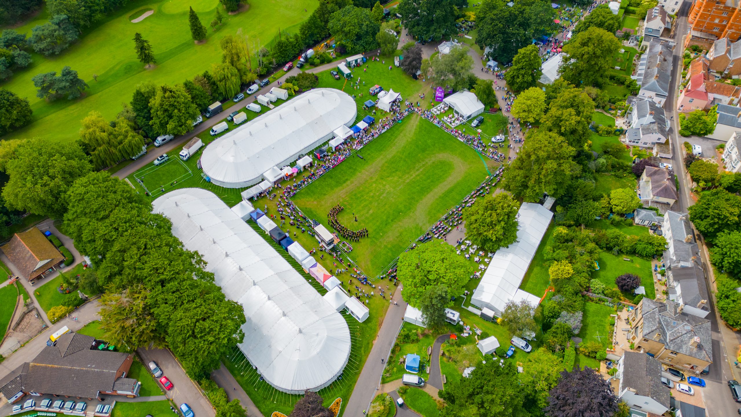Drone view of Vivary Park set up for Taunton Flower Show. The picture is taken above the competition marquee and shows the arena, the the Rock choir performing, crowds watching and a good view of the Floral Marquee. Views od the houses about Vivary Park on Mount St